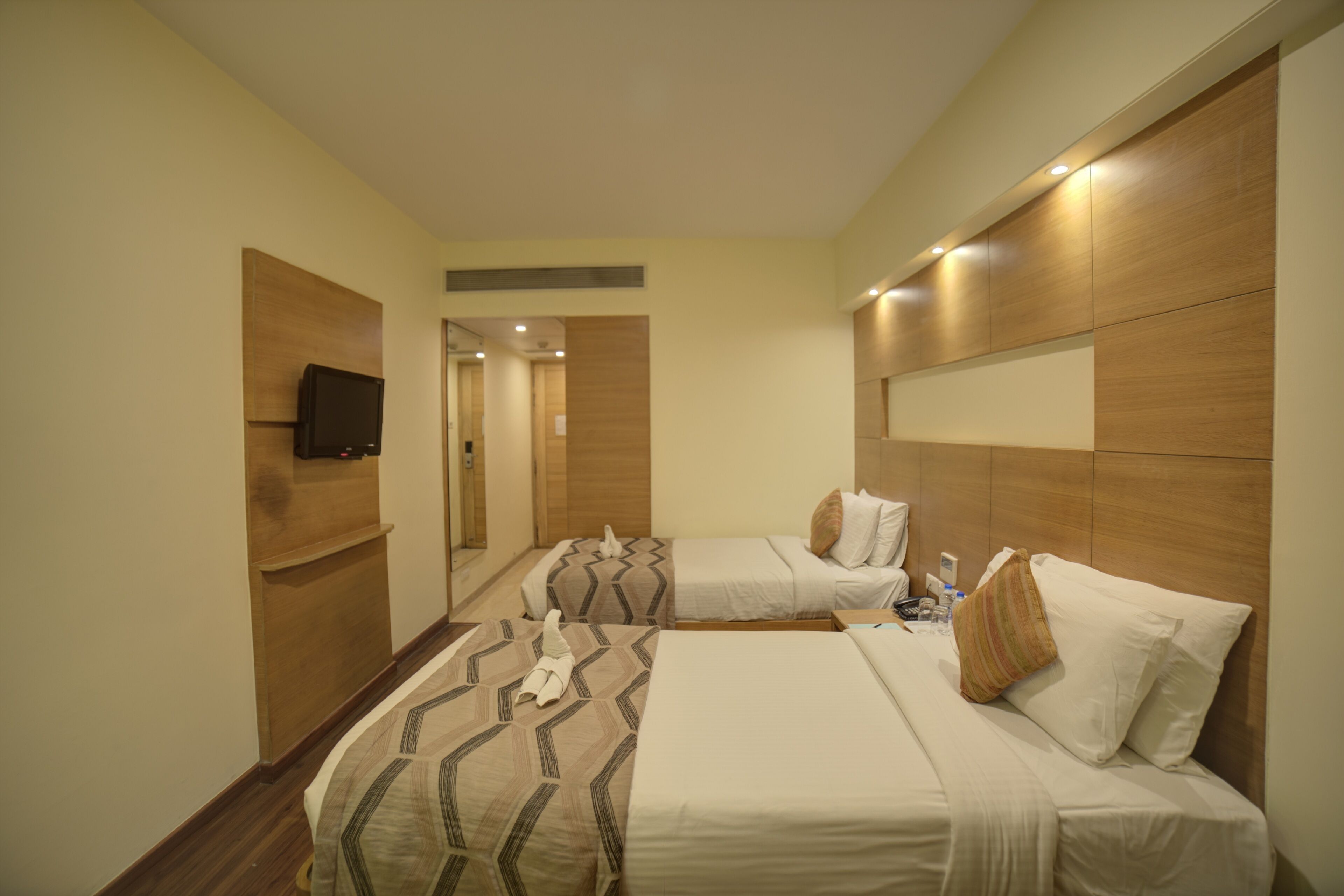 Habitación de hotel con dos camas, un televisor montado en la pared y un cabecero de madera.