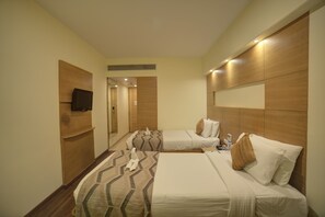 A hotel room with two beds, a television mounted on the wall, and a wooden headboard.