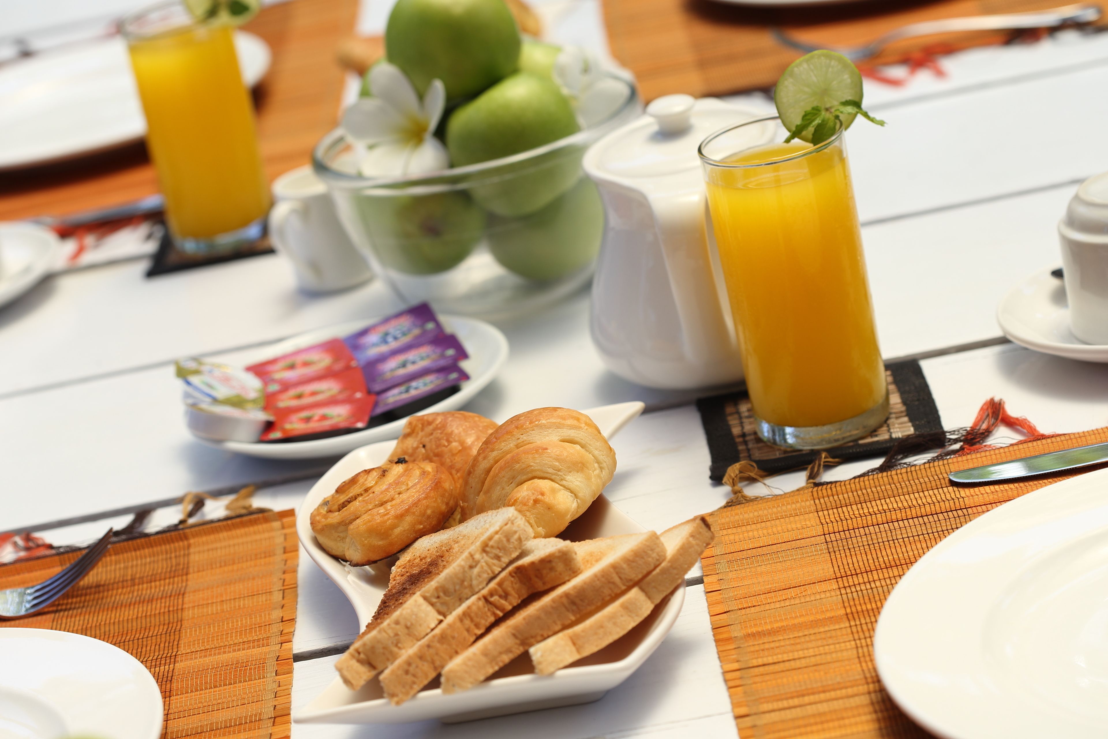 Une table mise pour le petit-déjeuner avec des croissants, du pain, un panier de fruits et un verre de jus d’orange.
