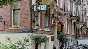 Un hotel con un letrero que dice "HOTEL", otro letrero que dice "Hotel Fita" y uno que dice "Van de Veldestraat". Hay bicicletas estacionadas afuera y un árbol en una maceta.