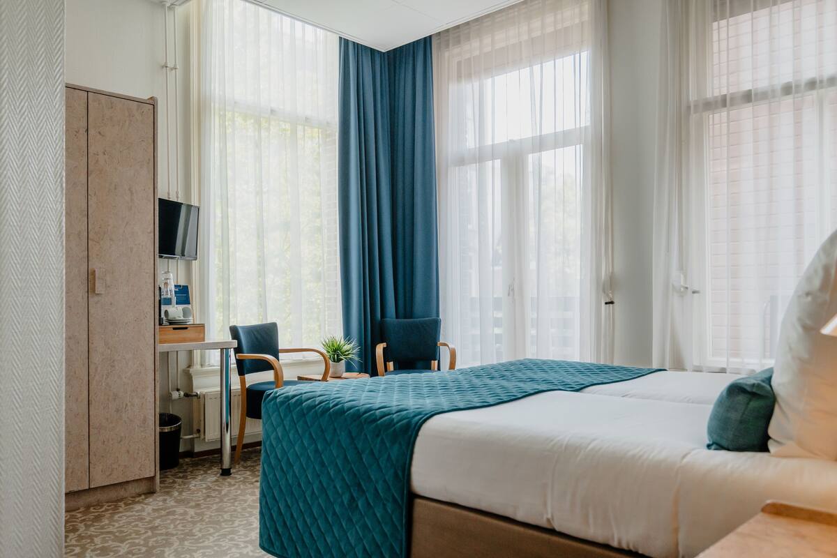 A hotel room with a bed, a desk, a chair, and a TV.