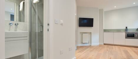 A modern bathroom with a glass shower, a white vanity, and a flat-screen TV mounted on the wall.