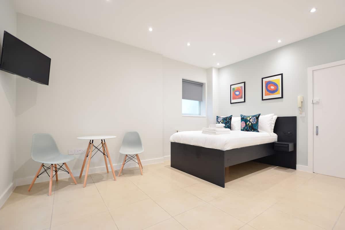 A modern bedroom with a bed, a small table, two chairs, a TV, and artwork on the wall.