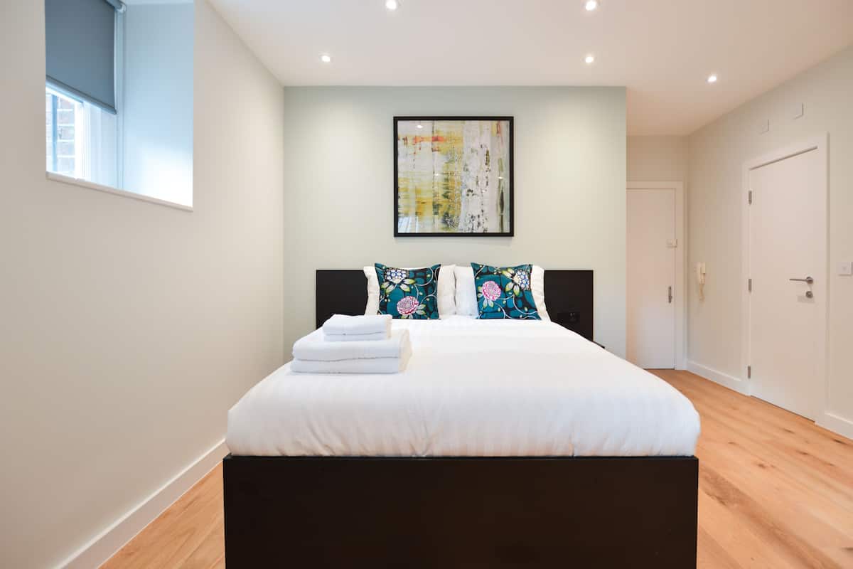 A bedroom with a bed, pillows, a framed artwork, and a window.