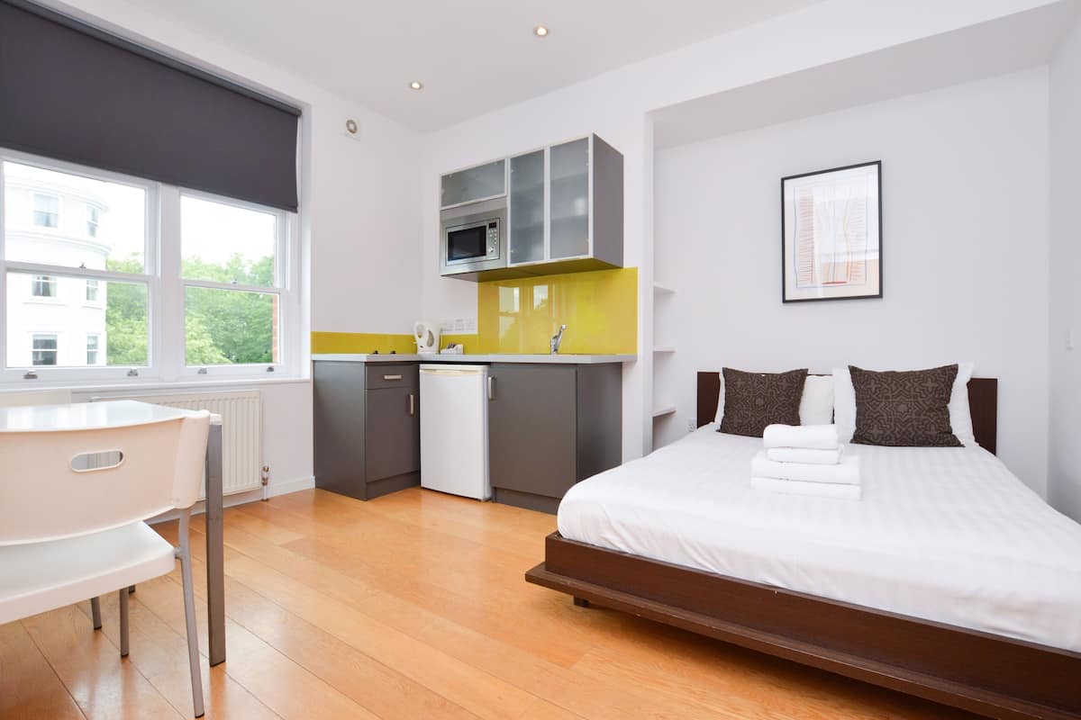 A modern bedroom with a large bed, a desk, and a kitchenette.