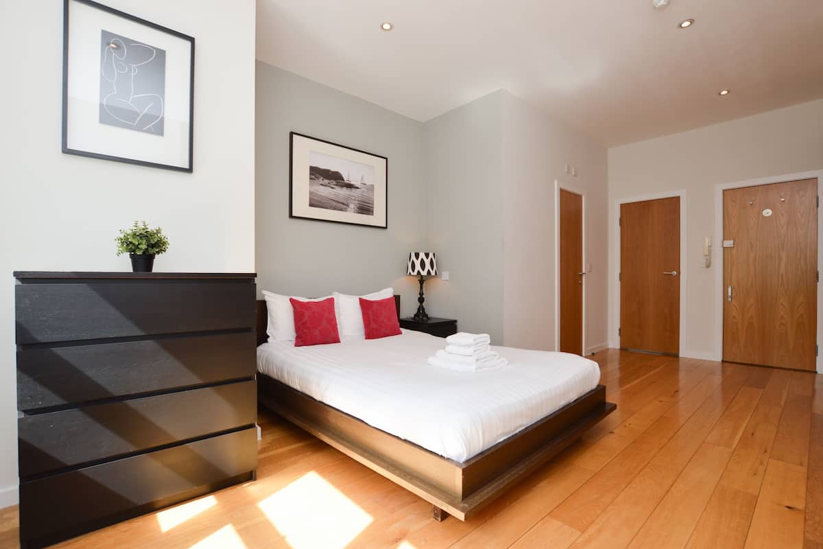 A modern bedroom with a large bed, a dresser, a framed picture, and a nightstand.