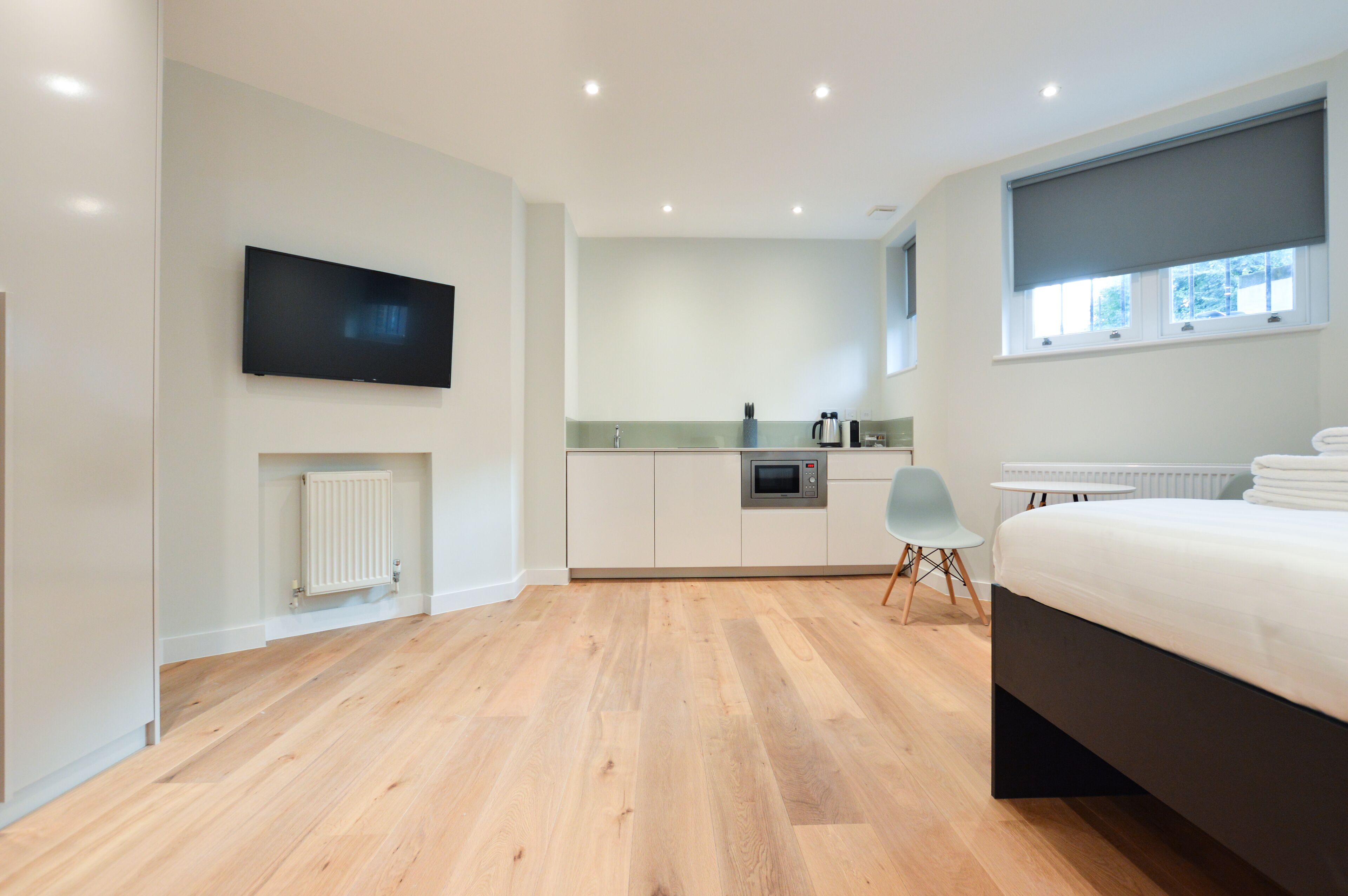 Un dormitorio moderno con una cama grande, un televisor de pantalla plana montado en la pared, una pequeña kitchenette y una ventana con vistas.