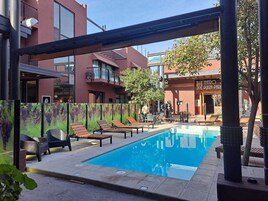 A swimming pool with lounge chairs, a pergola, and a view of a theater and plaza.