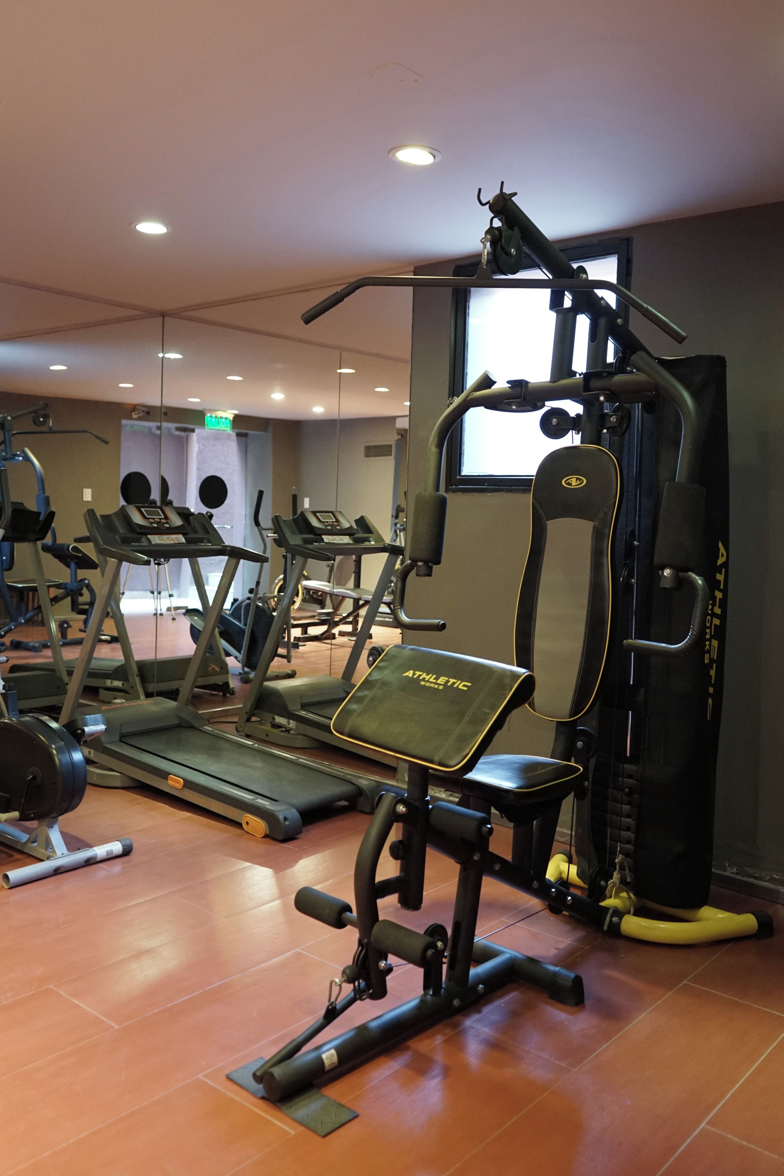Un gimnasio con diversos equipos de ejercicio, incluyendo cintas de correr, un banco de pesas y una estructura para sentadillas.