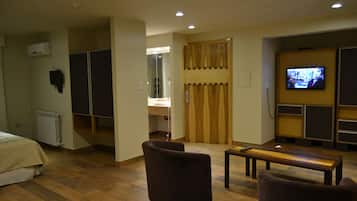 Een hotelkamer met een bed, twee fauteuils, een houten tafel, een televisietoestel, een kledingkast en een spiegel.