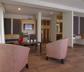 A modern living room with two patterned armchairs, a wooden coffee table, and a flat-screen TV mounted on the wall. - Plaza Paradiso by Camberland (Chacras de Coria)