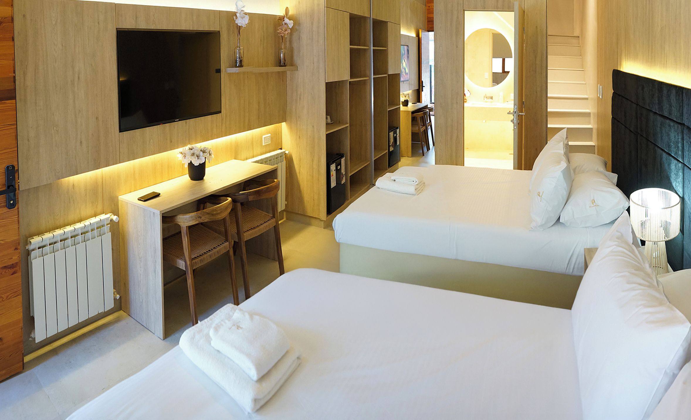 Habitación de hotel con cama, escritorio, silla, televisor y baño visible a través de una puerta abierta.