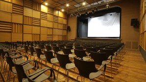 An auditorium with rows of chairs, a stage with a projection screen, and a wooden floor. - Plaza Paradiso by Camberland (Chacras de Coria)