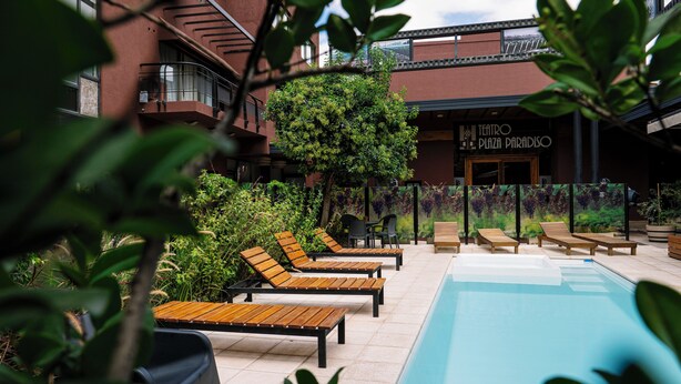 A poolside area with lounge chairs and a building with a sign reading "TEATRO PLAZA PARADISO". - Plaza Paradiso by Camberland (Chacras de Coria)