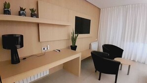 A modern living room with a long wooden desk, a black sofa, and a small black chair. There is a potted plant on the desk and a flat-screen TV mounted on the wall. - Plaza Paradiso by Camberland (Chacras de Coria)