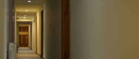 A narrow, dimly lit hallway with wooden doors and a carpeted floor.