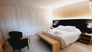 A modern hotel room with a bed, a bench, a chair, and a bedside table. - Plaza Paradiso by Camberland (Chacras de Coria)