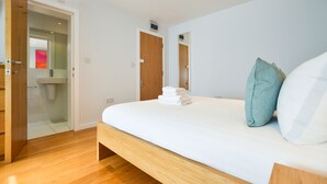 Une chambre à coucher avec un lit en bois, une salle de bain visible à travers une porte ouverte et un miroir sur le mur.