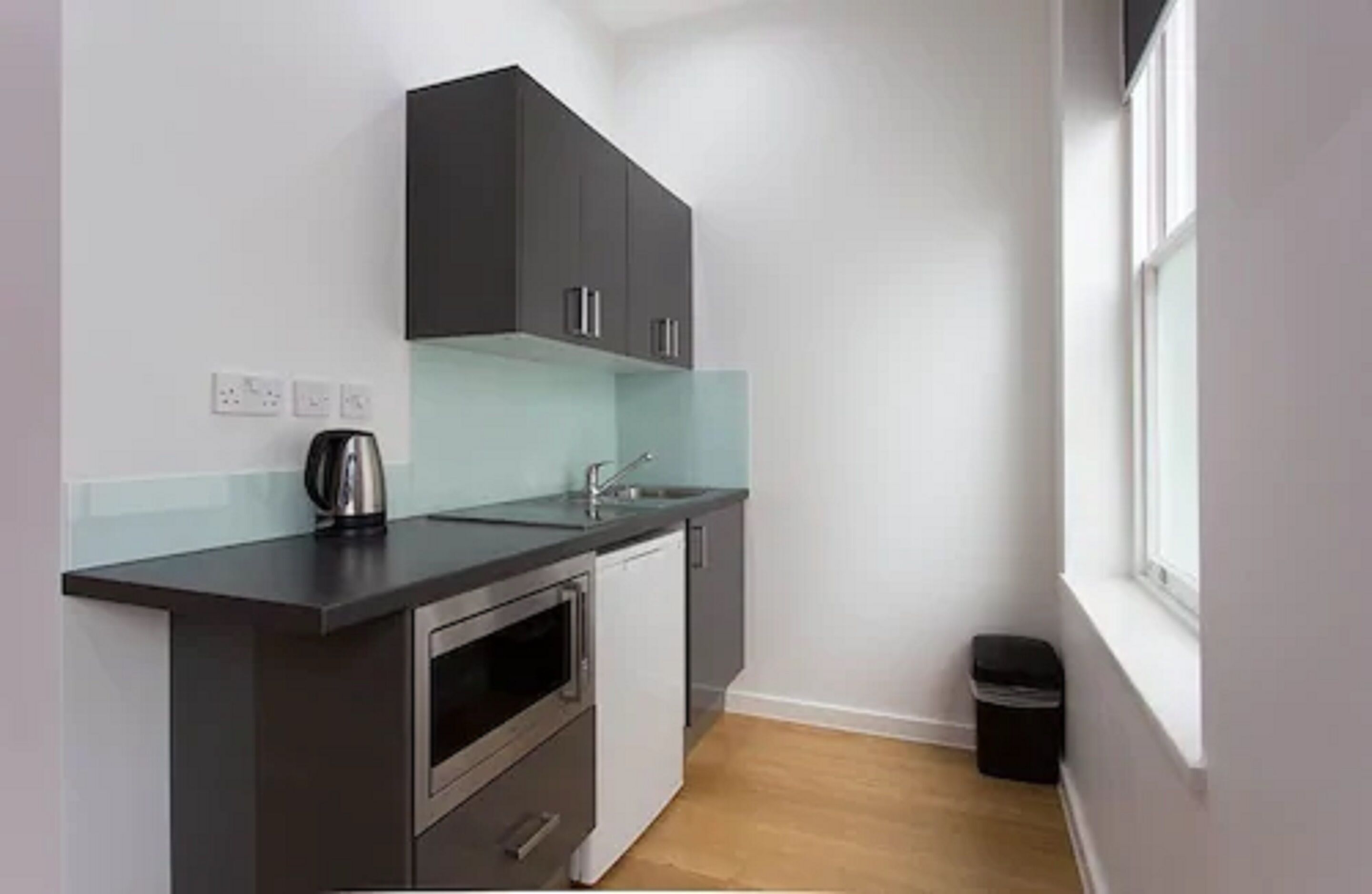 A compact kitchen with dark cabinets, a stainless steel sink, and a small oven.