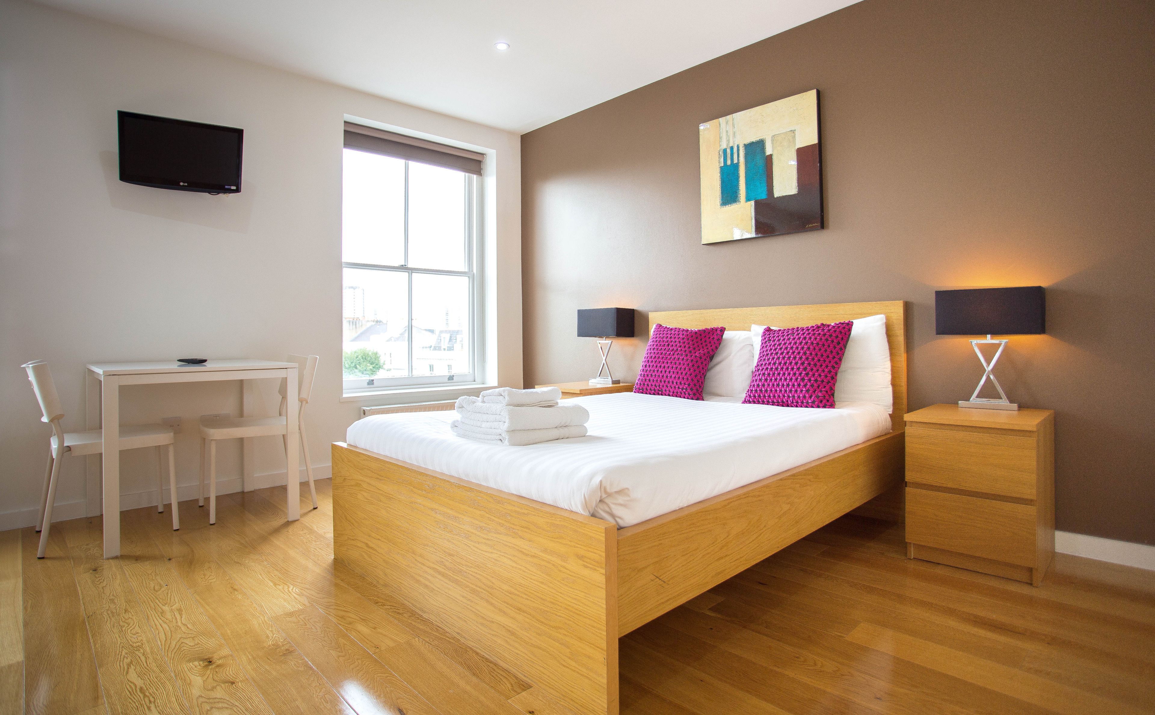 A modern hotel room with a wooden bed, a desk, and a chair.