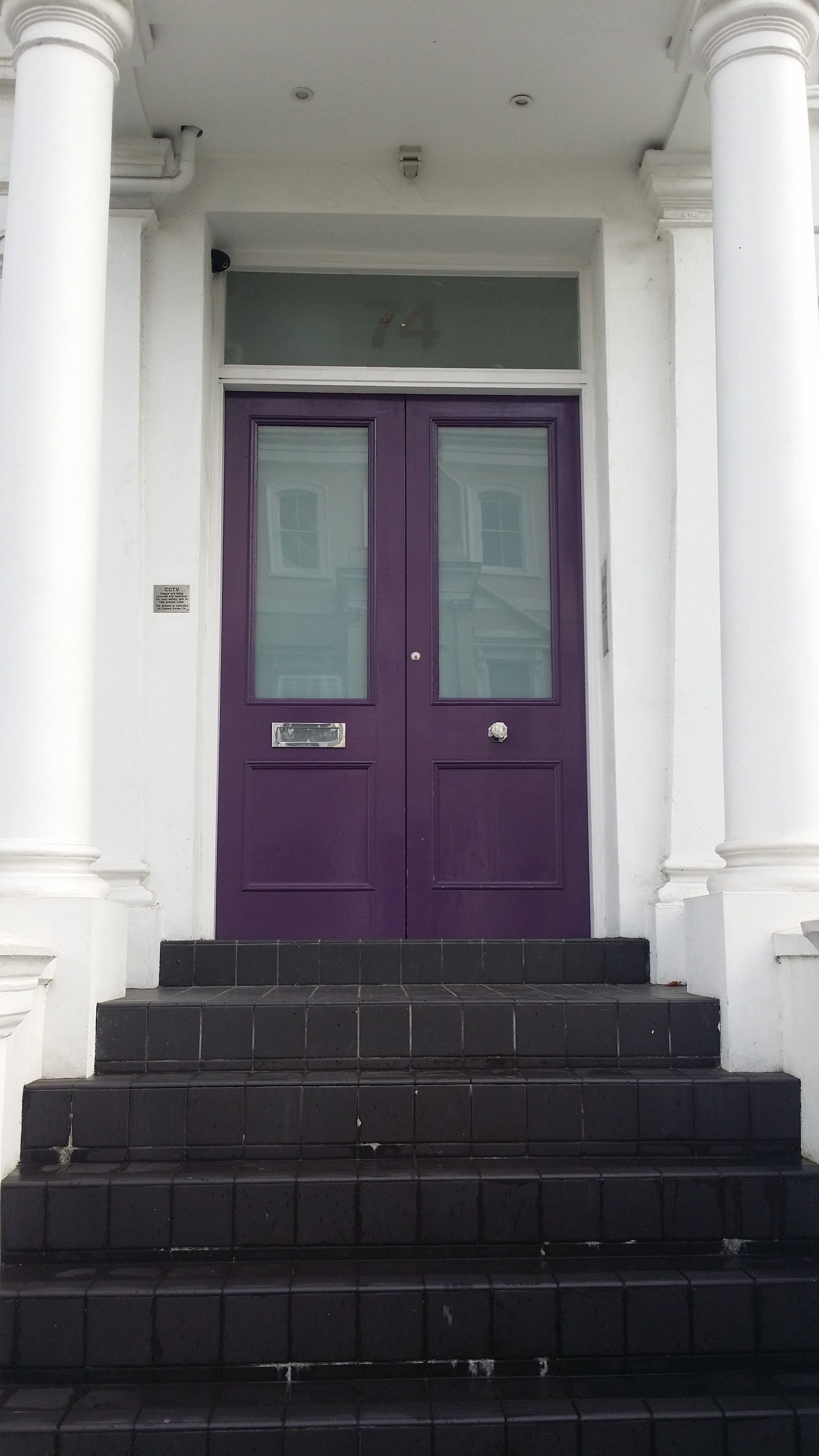A purple double door with a small window, flanked by white columns, leading to a set of black steps.