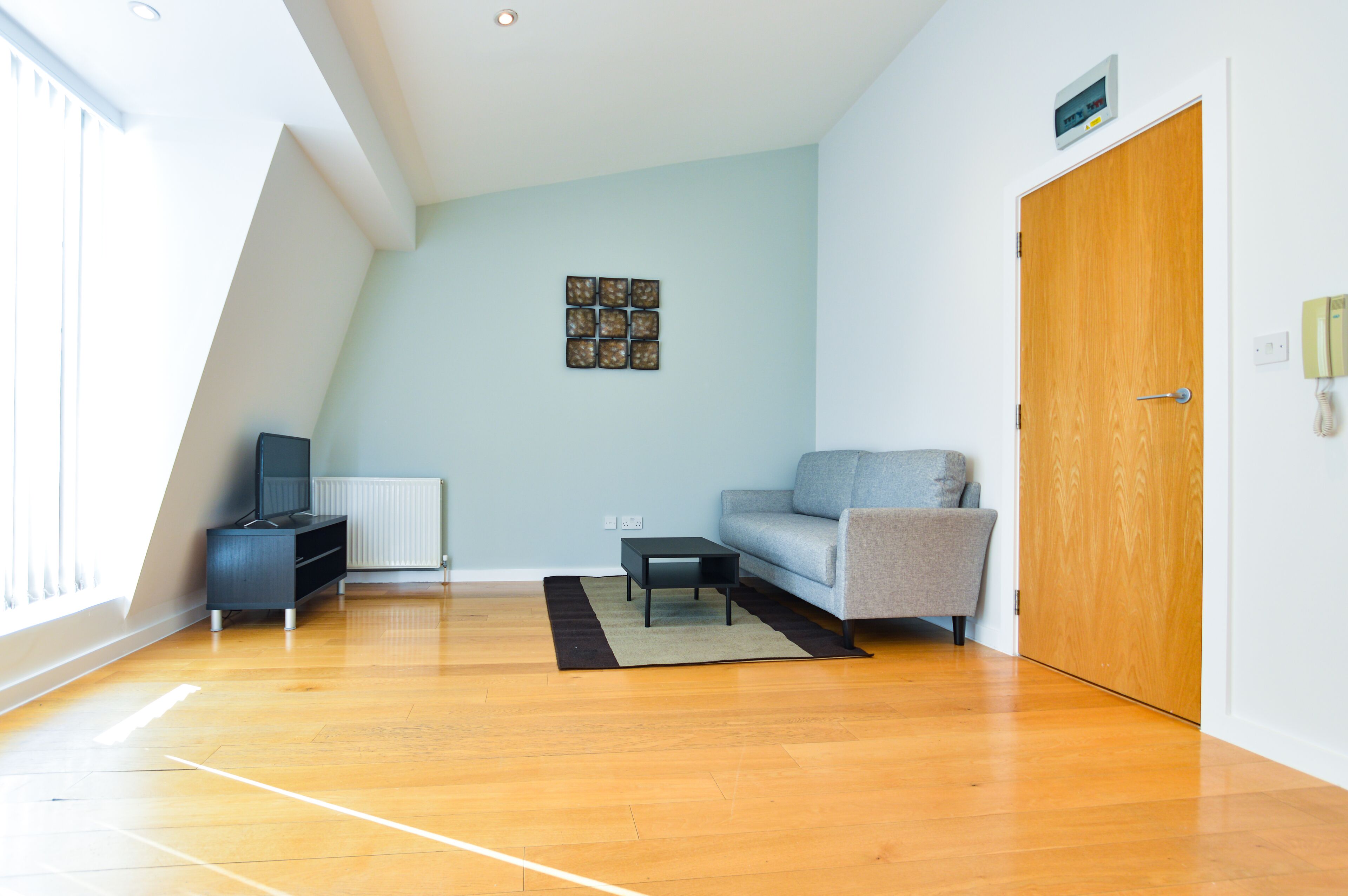A modern living room with a wooden floor, a grey sofa, a black coffee table, and a small black TV stand.