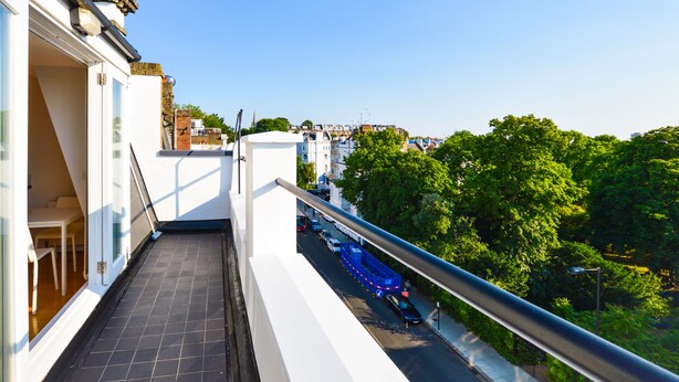 Un balcon donnant sur une rue de la ville et sur un espace verdoyant.