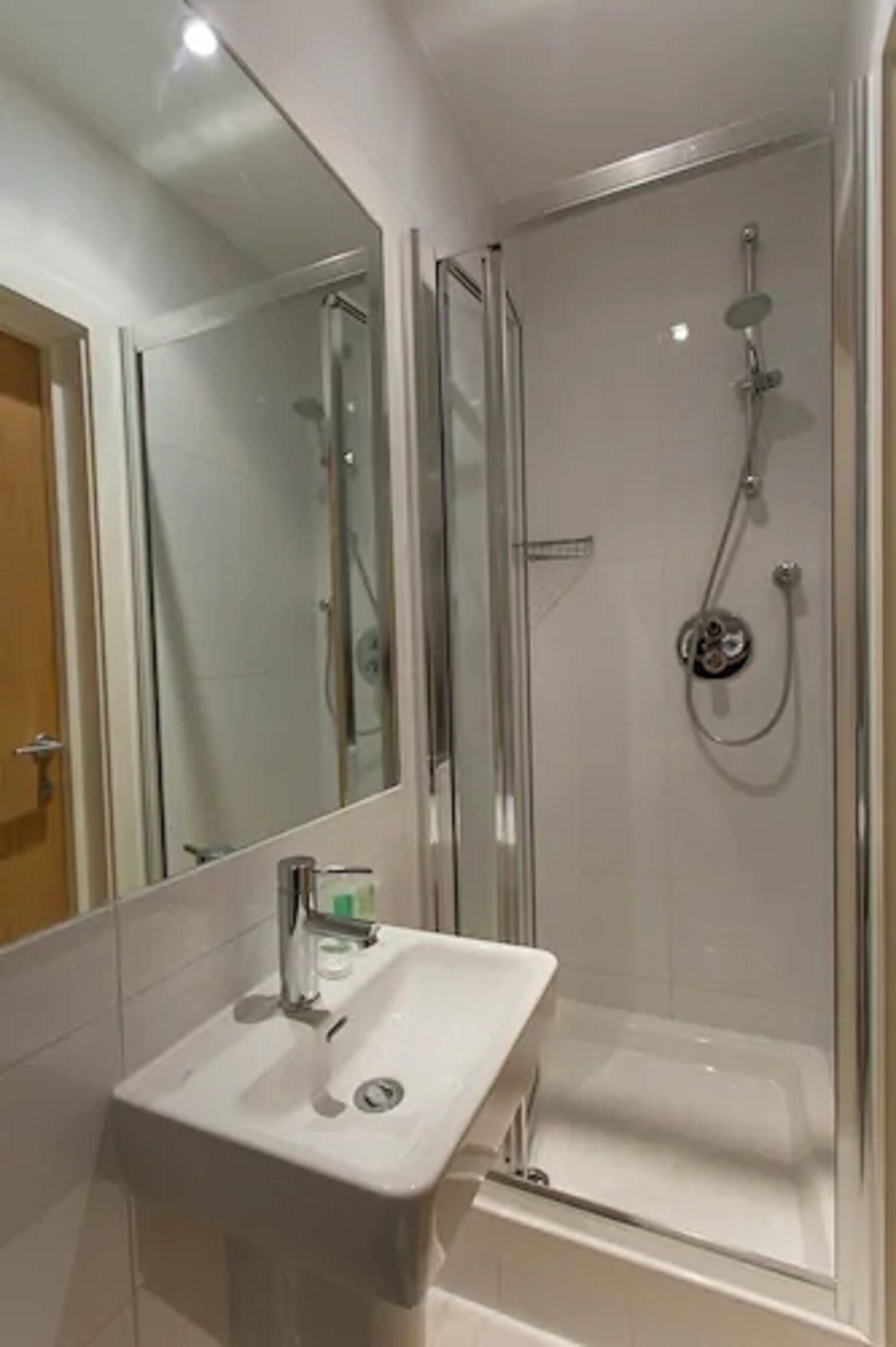 Et moderne badeværelse med et glasafskærmet brusebad, en hvid vask og et stort spejl.