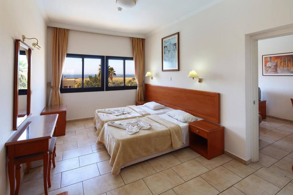 Habitación de hotel con dos camas, un escritorio y una silla. Se ve el mar a través de la ventana.