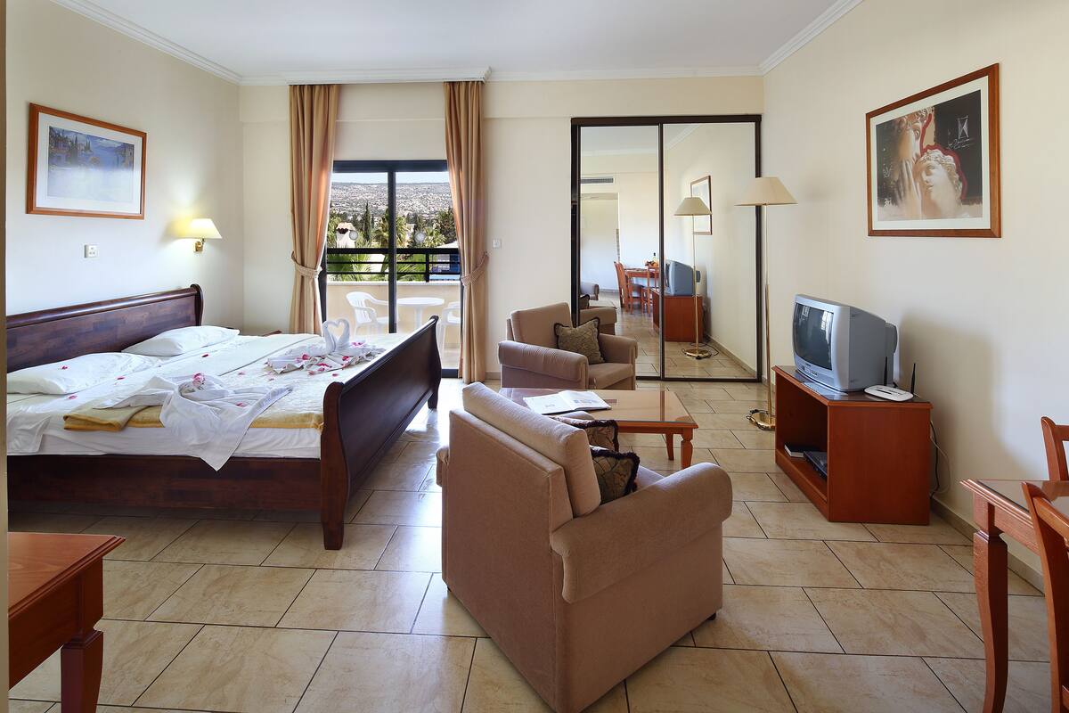 Habitación de hotel con cama, sofá, televisión y balcón con vistas.
