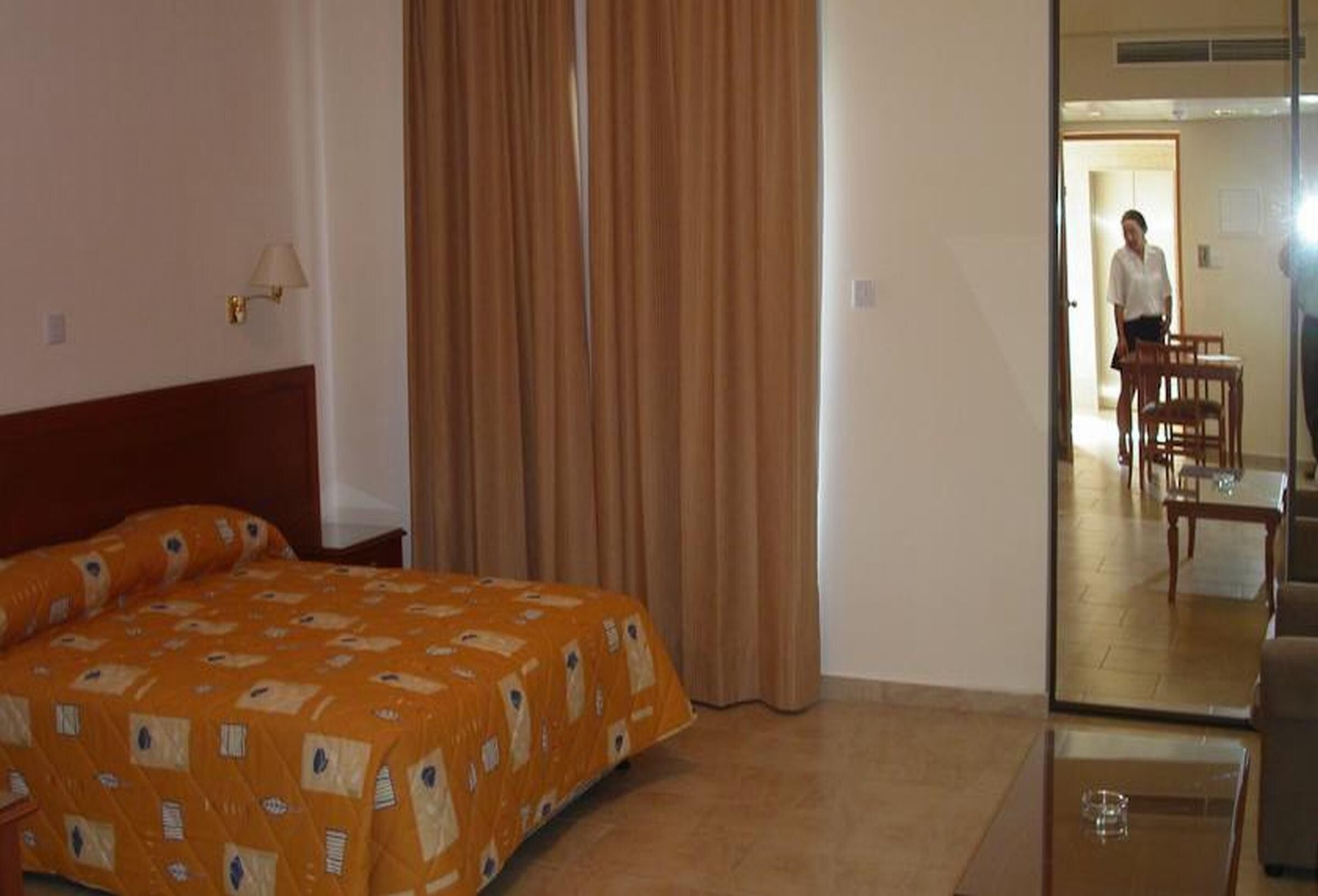 A hotel room with a bed, a mirror, a wooden chair, and a table.