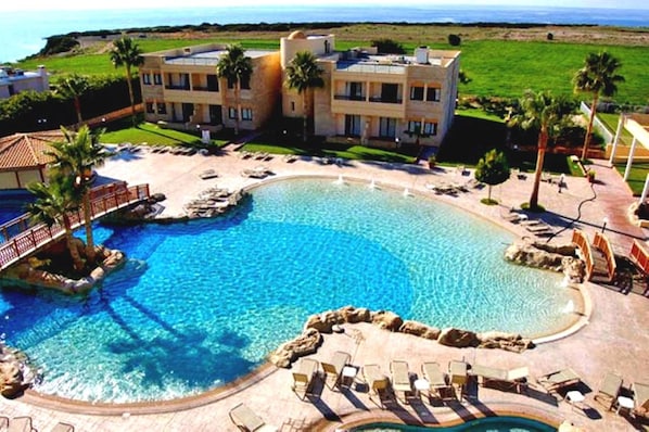 A resort with a large pool, palm trees, and a view of the ocean. - Panareti Coral Bay Resort (Pegeia)
