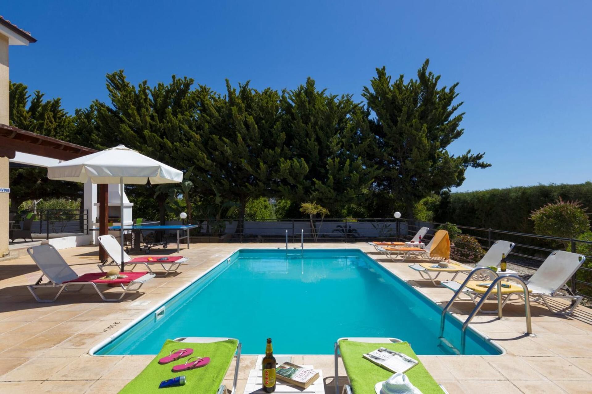 Un área de piscina con sillones de descanso, una mesa y sombrillas.