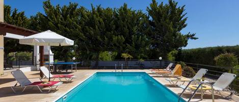 Un área de piscina con sillones de descanso, una mesa y sombrillas.