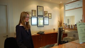En receptionsdisk med inramade certifikat på väggen, en dator och en skrivare.