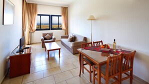 Una sala de estar con un sofá, una mesa de comedor con sillas, un televisor y un ventanal con vistas al paisaje.