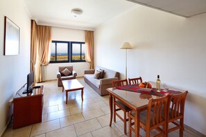 Ein Wohnzimmer mit einer Couch, einem Esstisch mit Stühlen, einem Fernseher und einem Fenster mit Landschaftsblick.