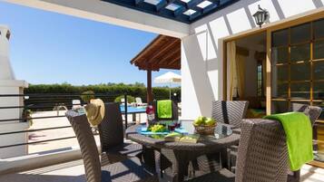 Une terrasse extérieure avec des meubles en osier, une table garnie de fruits et de boissons, et une vue sur la mer.
