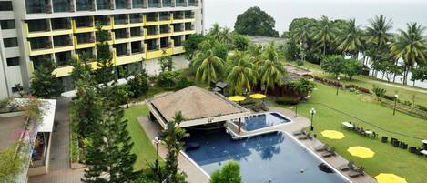 A hotel with a swimming pool, palm trees, and a view of the ocean.