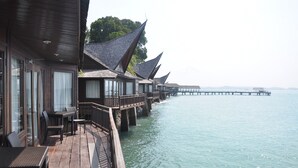 Overwater bungalows with wooden decks and railings, connected by a wooden walkway over calm water. - Batam View Beach Resort (Batam)
