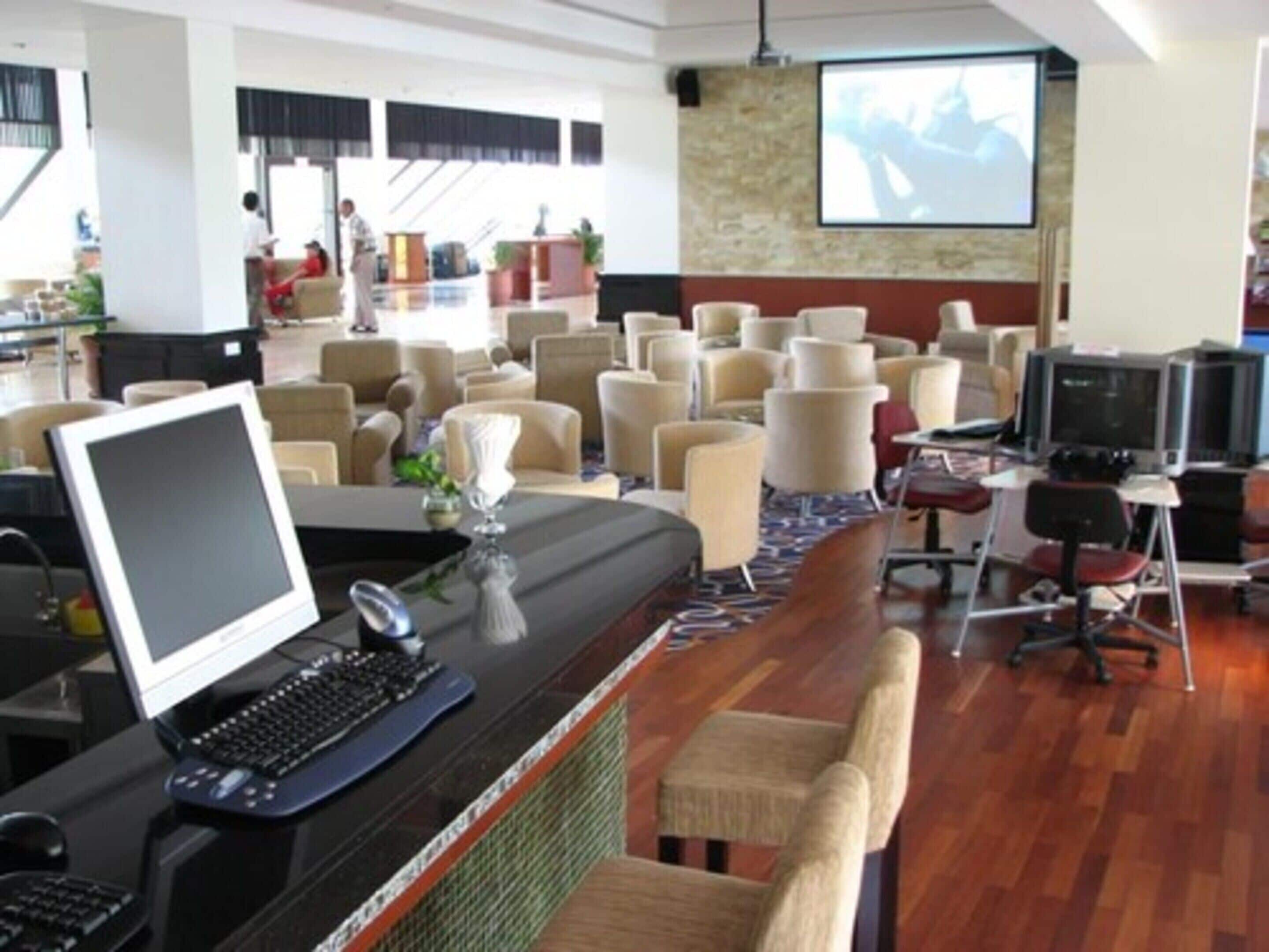 Uma sala de conferências com uma tela grande, várias cadeiras, uma mesa com um computador e um projetor.