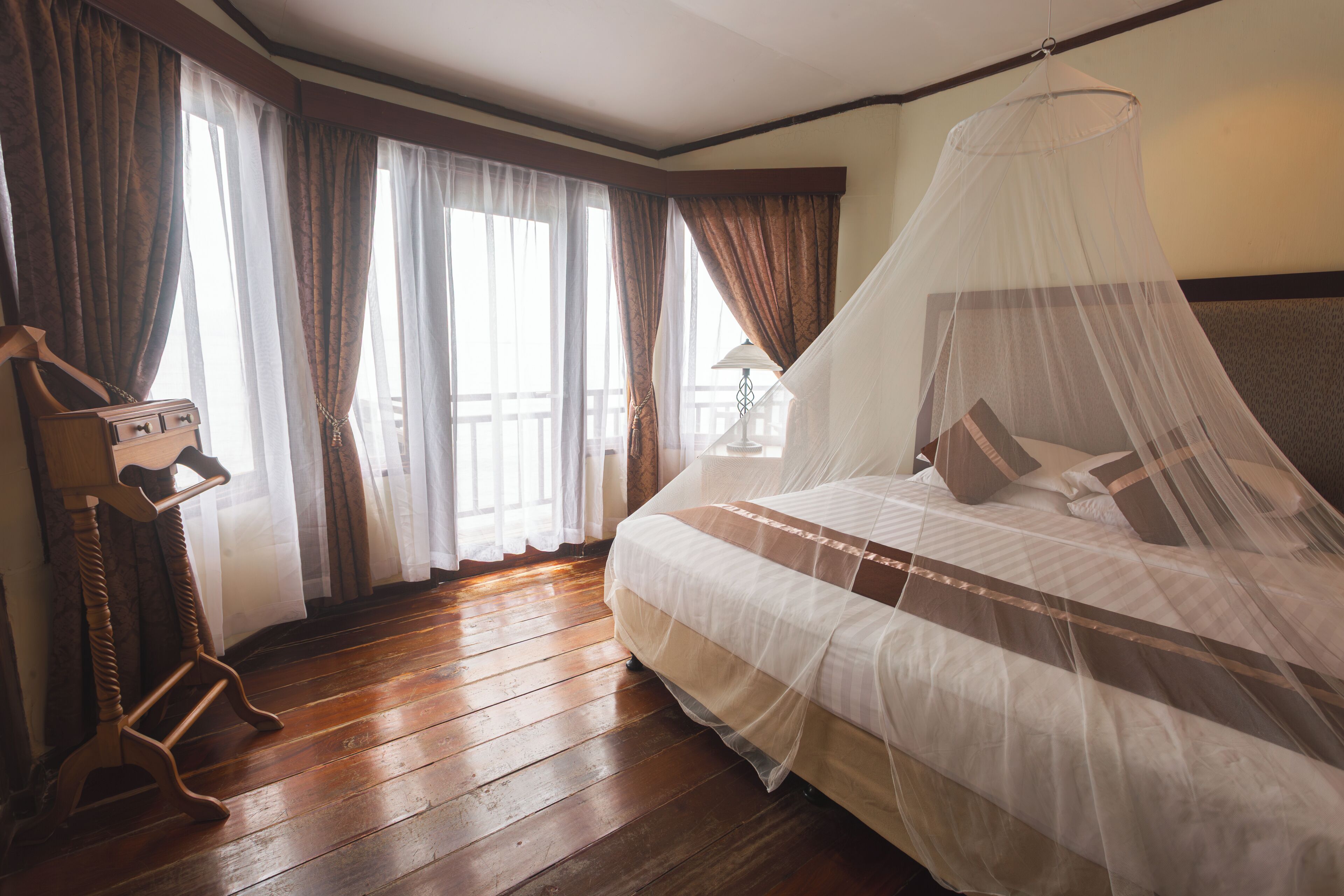 Een slaapkamer met een bed, gordijnen, een houten vloer en een nachtkastje.