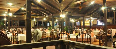 A spacious restaurant with multiple tables and chairs, high ceilings, and hanging lights.