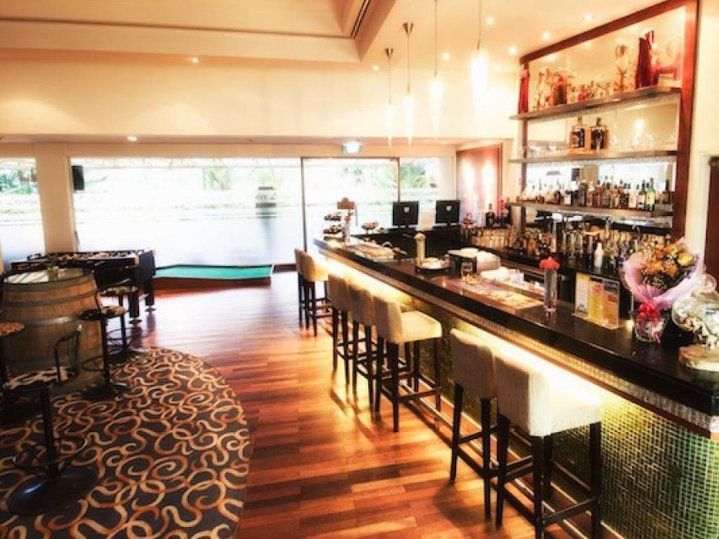 Zona de bar con suelo de madera, taburetes y barra.