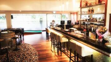 Zona de bar con suelo de madera, taburetes y barra.