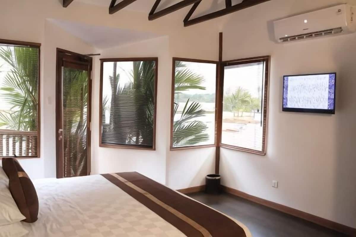 Ein Schlafzimmer mit Bett, großen Fenstern, einem Fernseher und einer Tür zu einem Außenbereich.