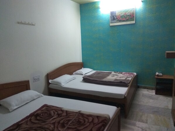 A room with two beds, a small table, and a wall-mounted picture. - Hotel Ganga Kripa (Jaipur)