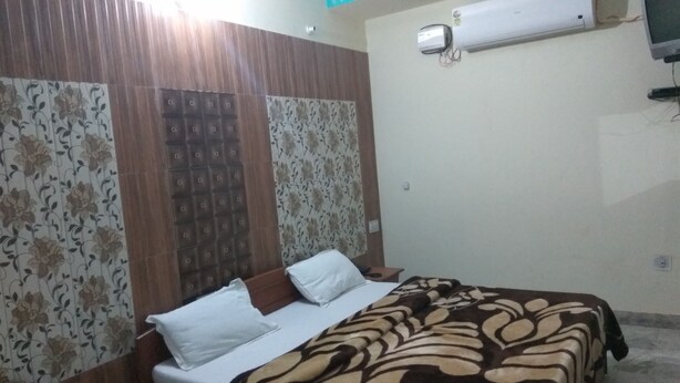 Un dormitorio con cama, almohadas, un edredón estampado, un aire acondicionado de pared y una cortina con motivos florales.