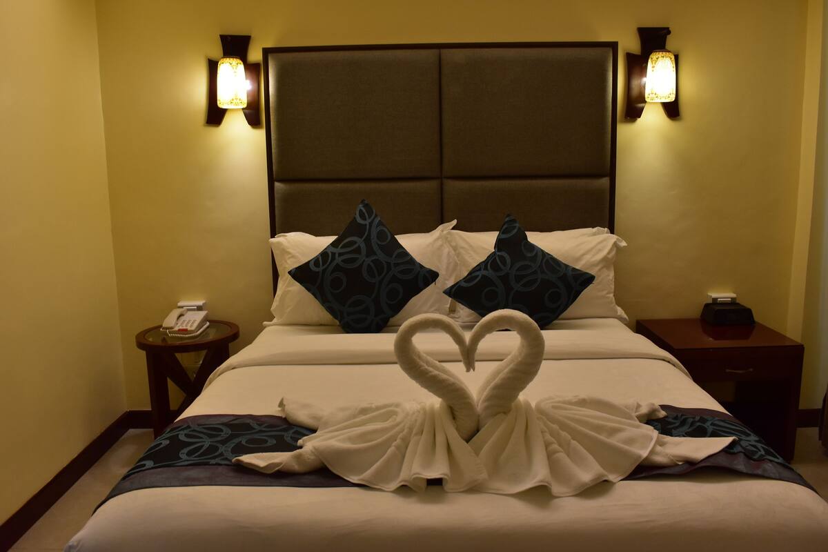 Een hotelkamer met een groot bed, twee nachtkastjes en een wandlamp.