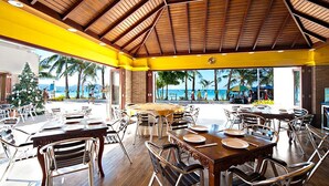 A restaurant with outdoor seating overlooking a beach, featuring wooden tables and chairs, and a view of palm trees and the ocean. - Golden Phoenix Hotel Boracay (Boracay Island)